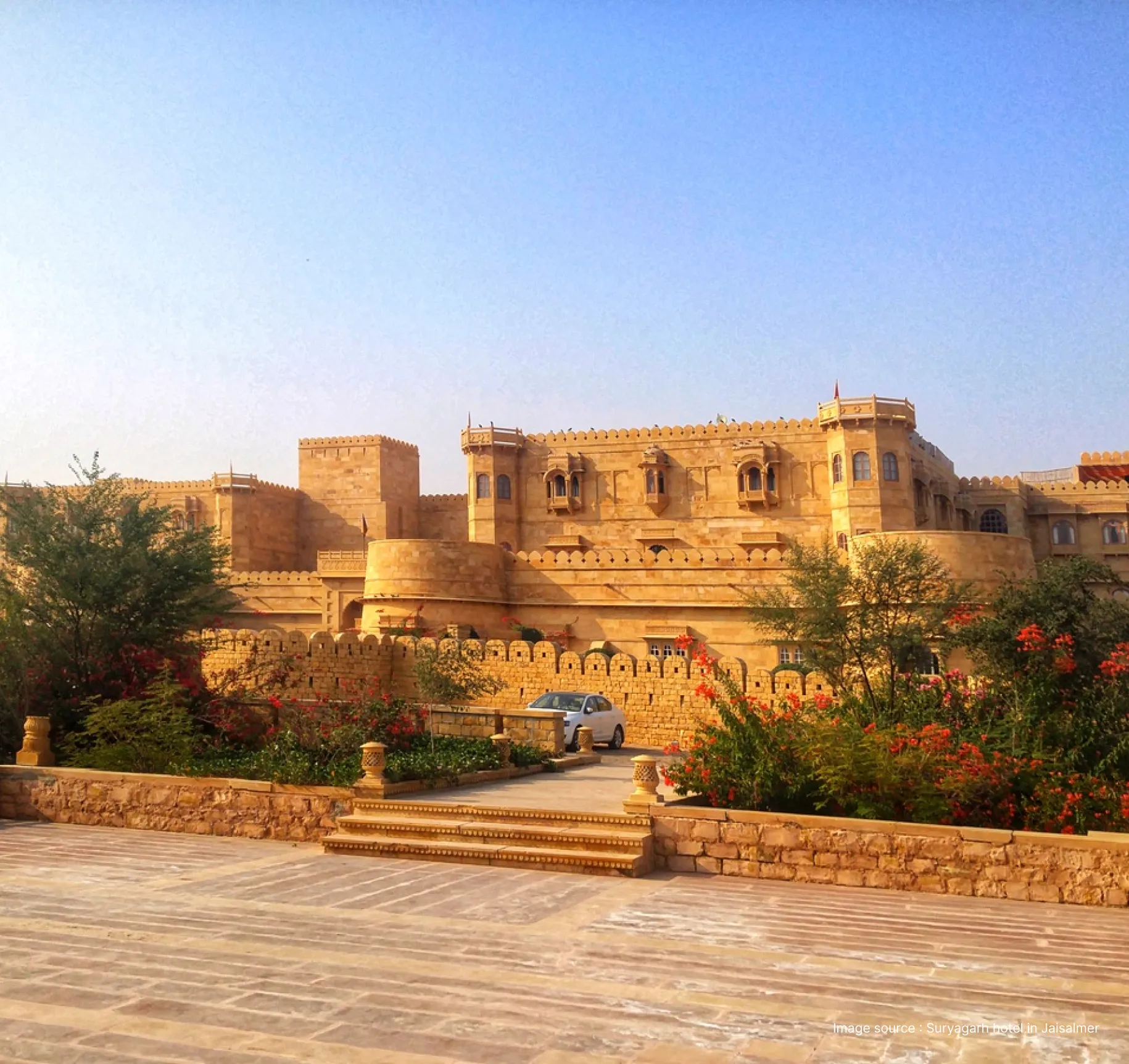 The majestic golden sandstone facade and lush gardens of the luxury Suryagarh hotel in Jaisalmer.