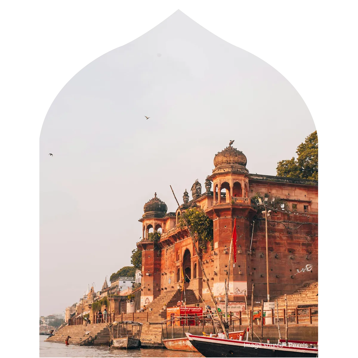 A scenic view of the red stone heritage buildings and boats at Dashashwamedh Ghat in Varanasi, framed through a traditional arched border.