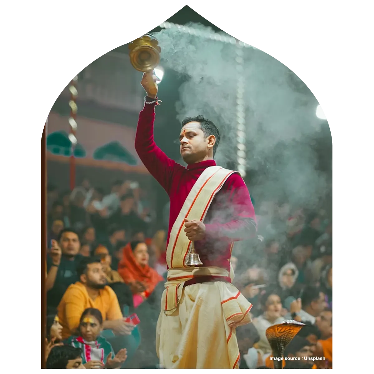 a pandit dressed in traditional clothes performs worship as devotees seated in the back watch