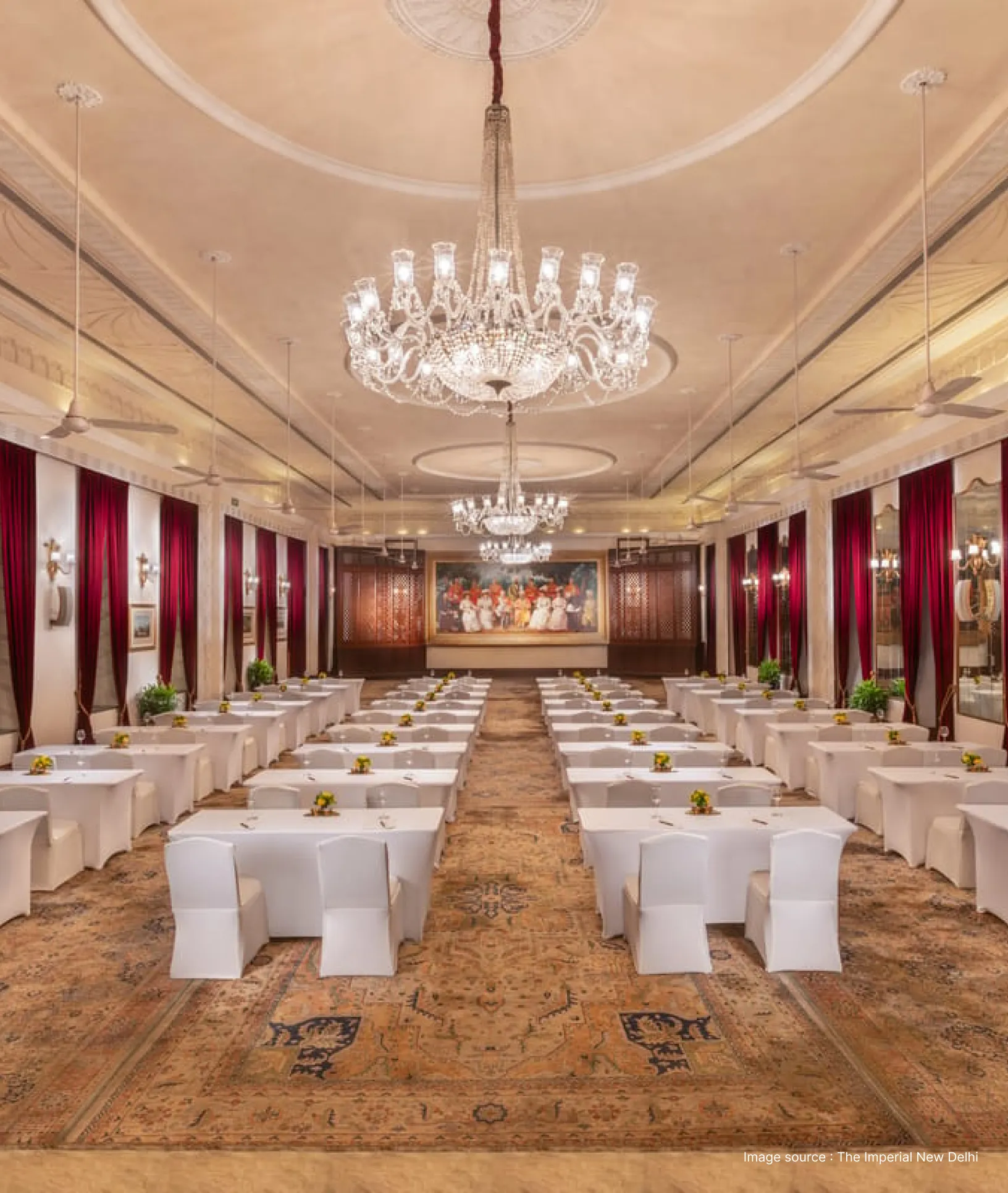 a long meeting hall with a beautiful lit up chandelier with white chairs
