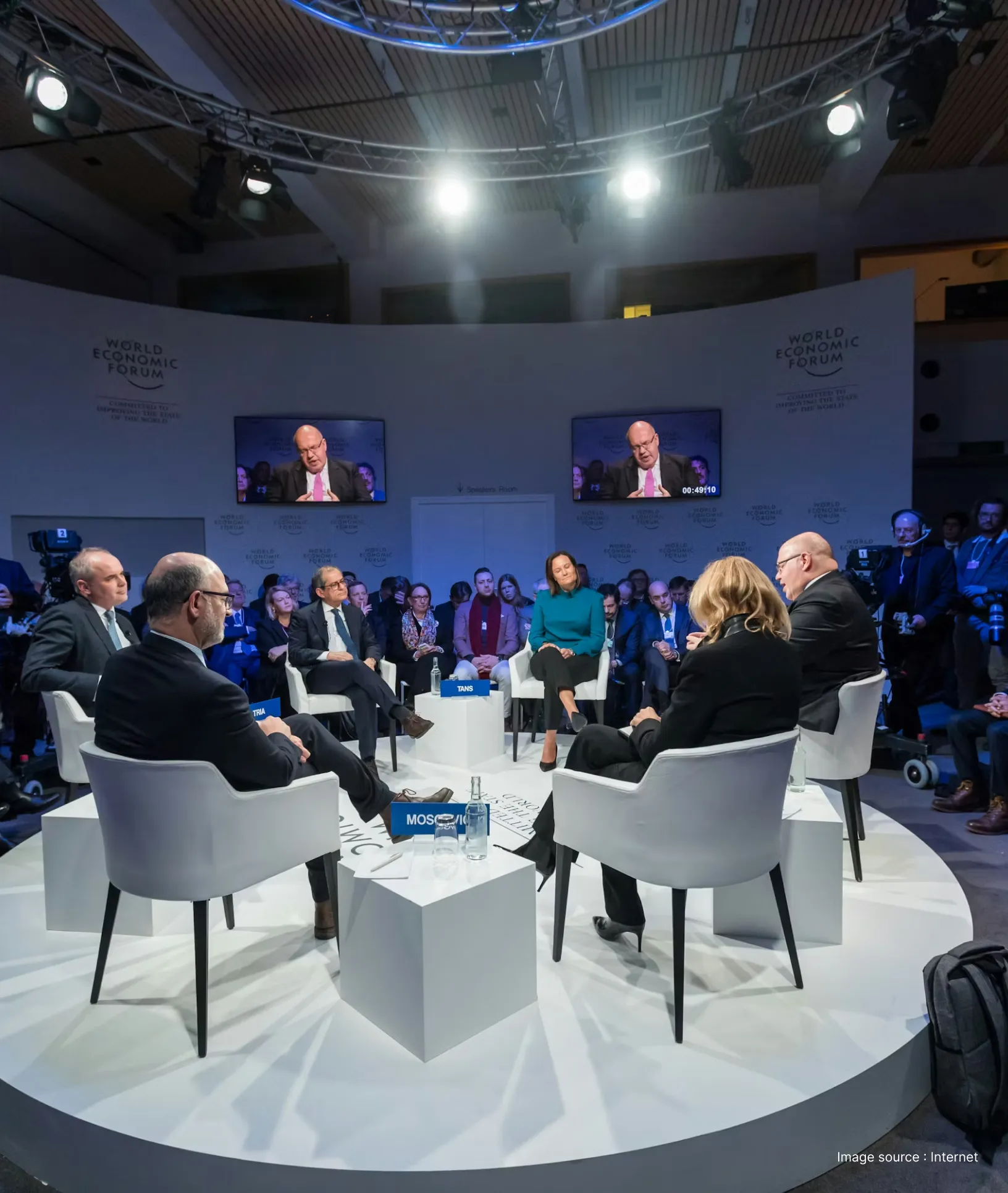 business professionals seated on stage on white chairs at an event