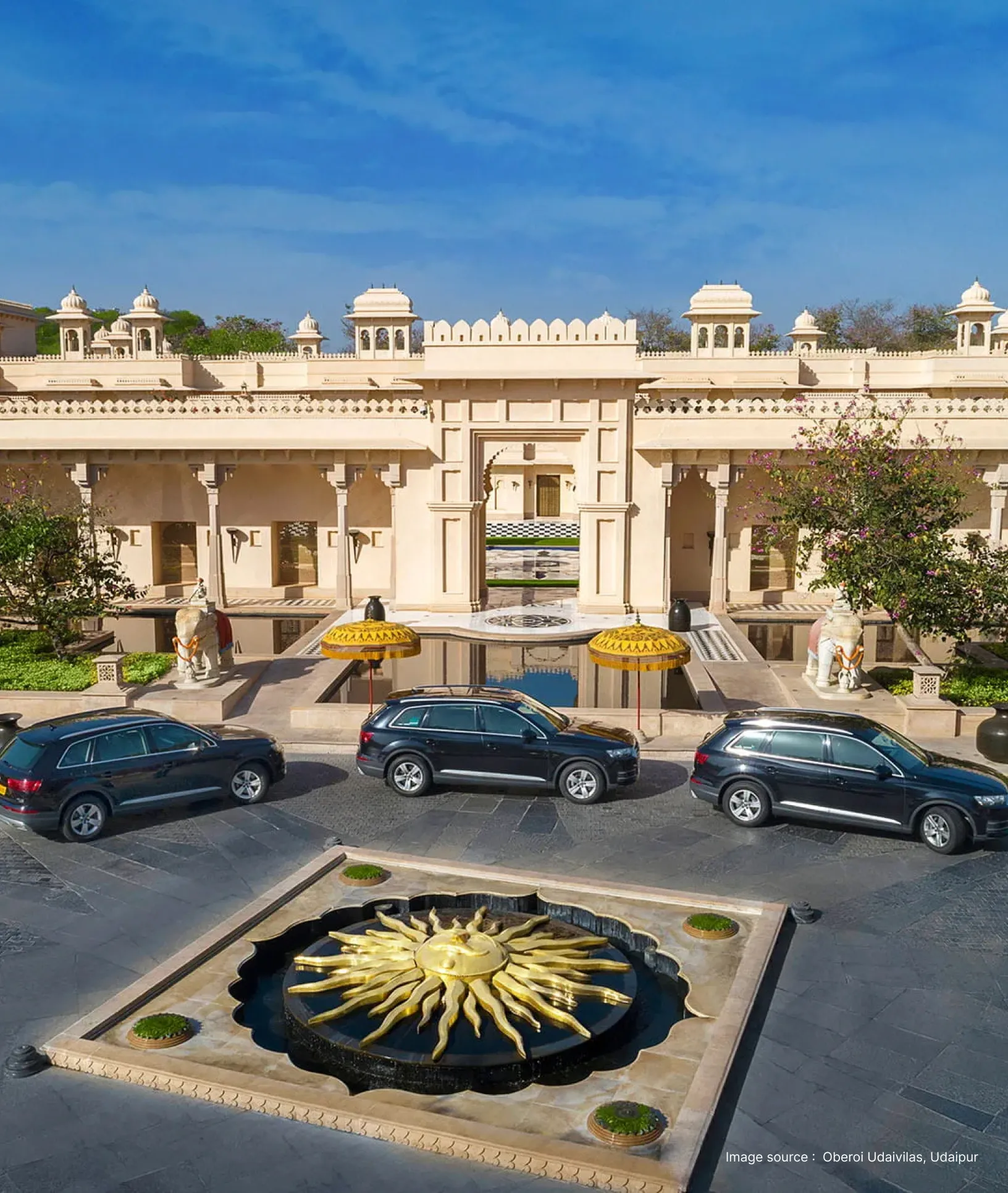 entrance of the oberoi udaivilas hotel with a striking sun statue and luxury cars