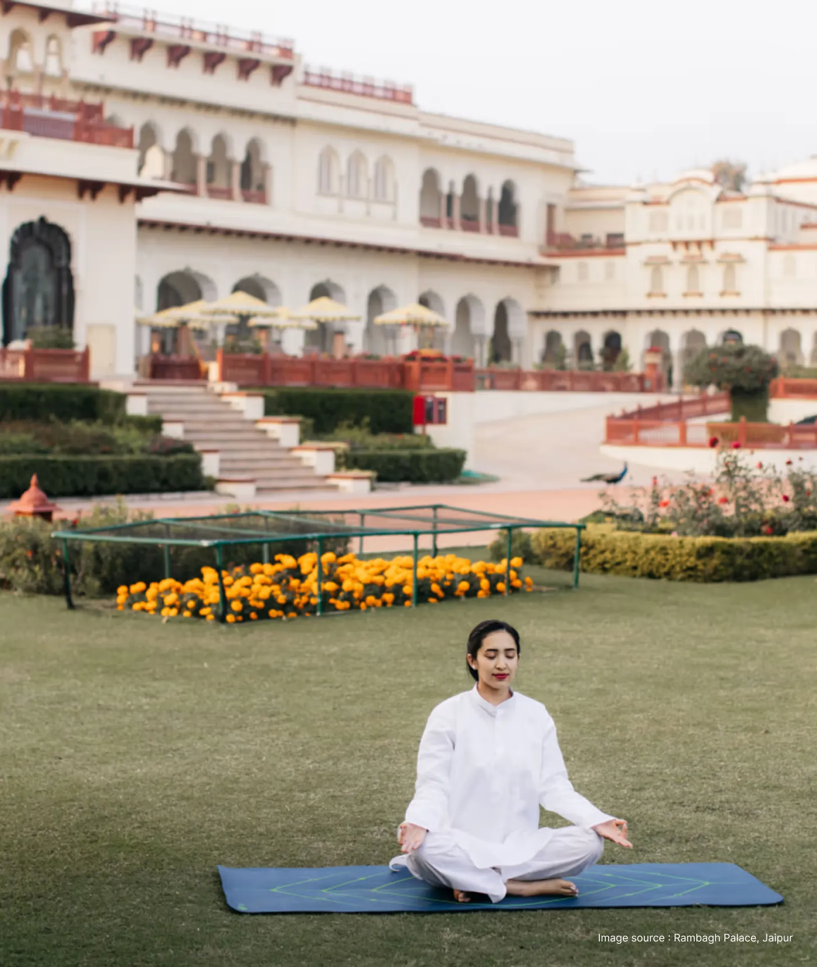 a woman dressed in a white kurta practicing meditation on a yoga mat in a serene garden at the rambagh palace