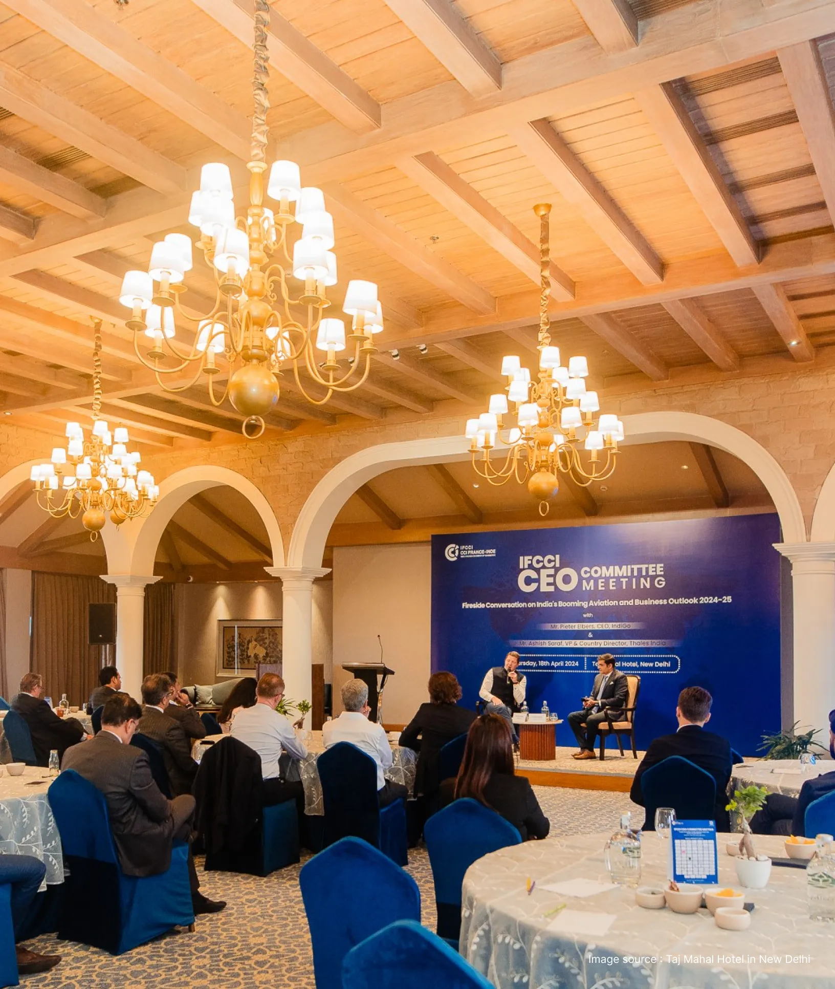 a conference underway at taj mahal hotel with round tables and a golden chandelier