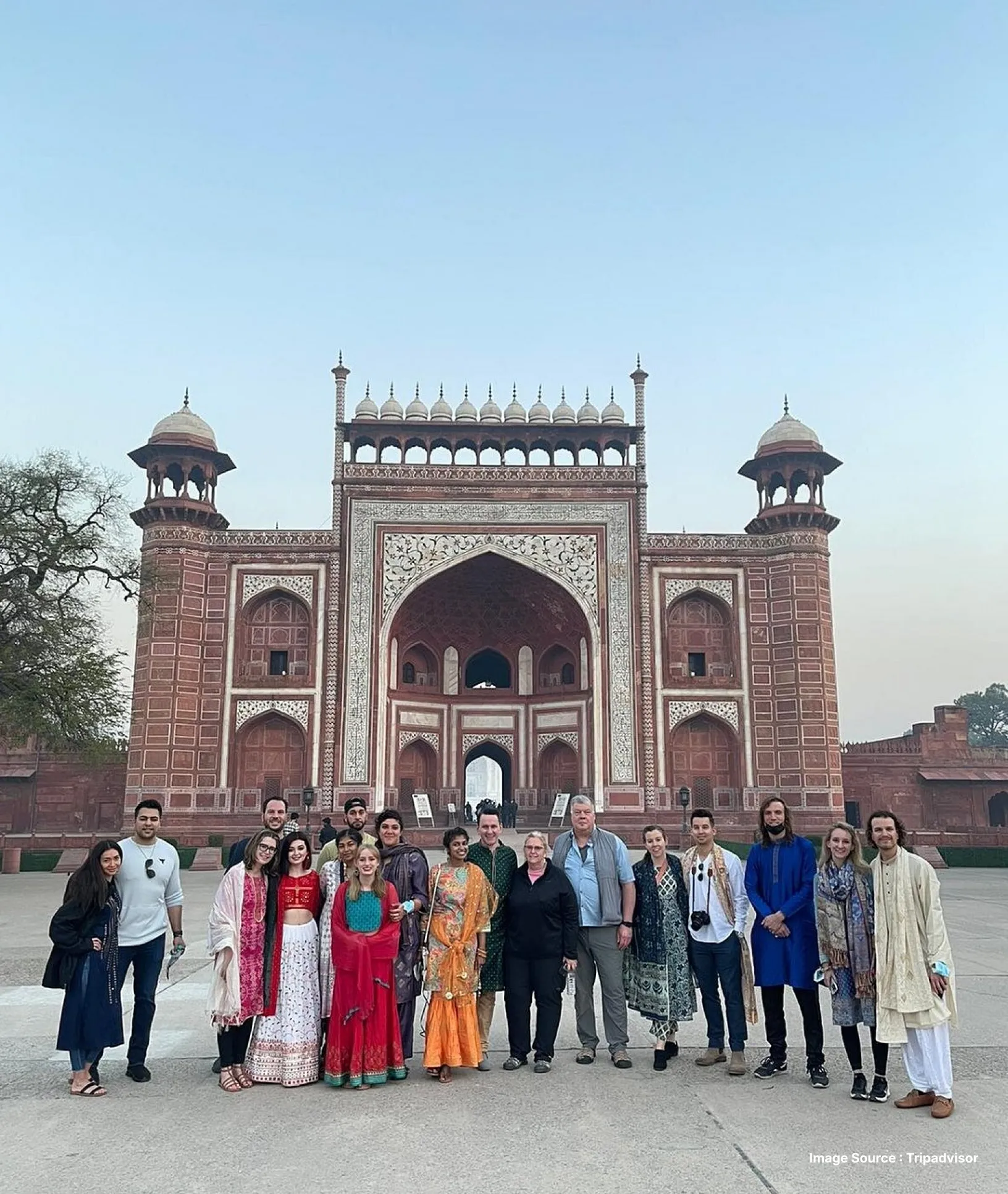 a group of tourists pose in traditional indian clothes at the taj mahal's red sandstone gate during daytime