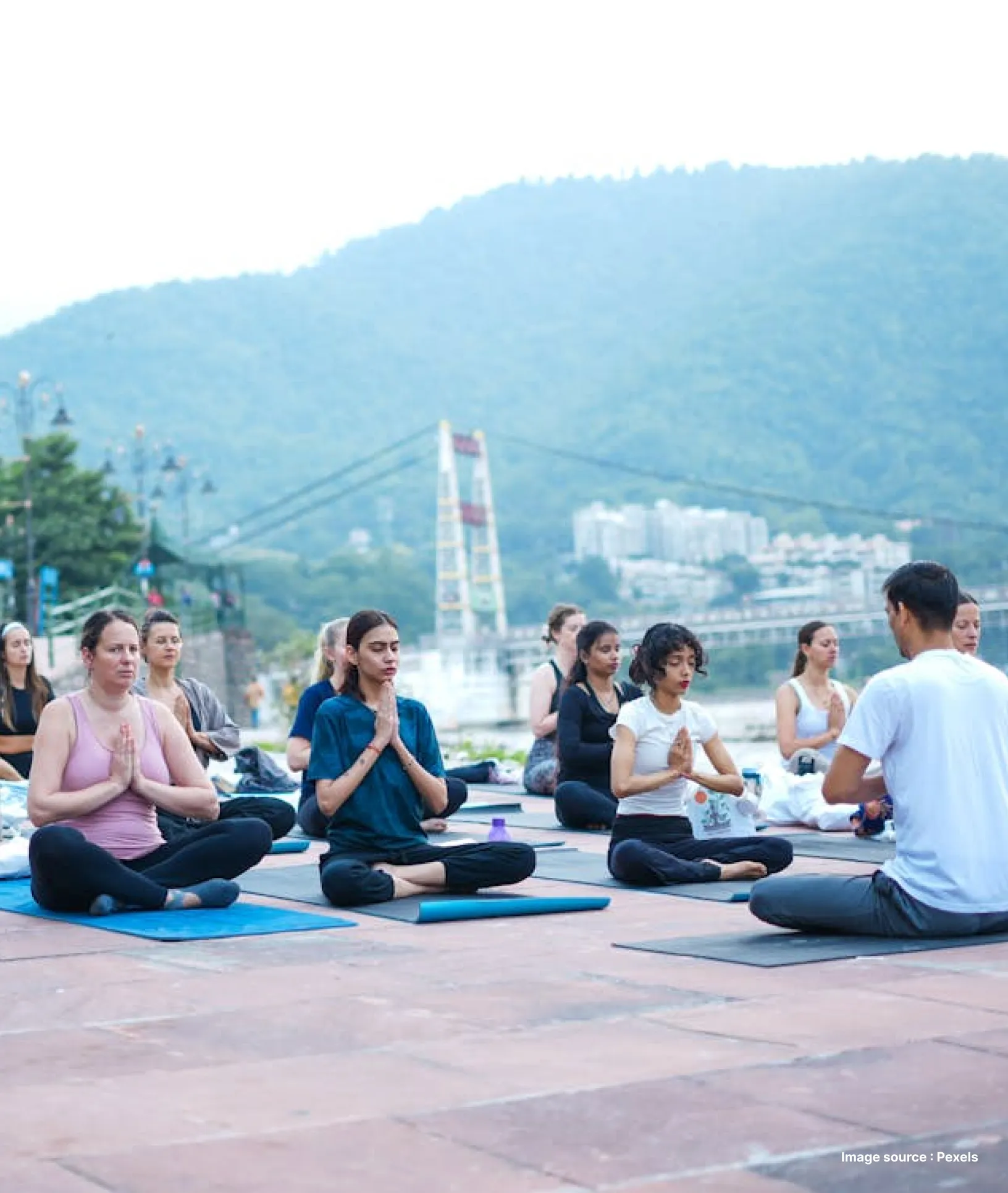 a group yoga session underway in rishikesh with lush green mountain in the backdrop