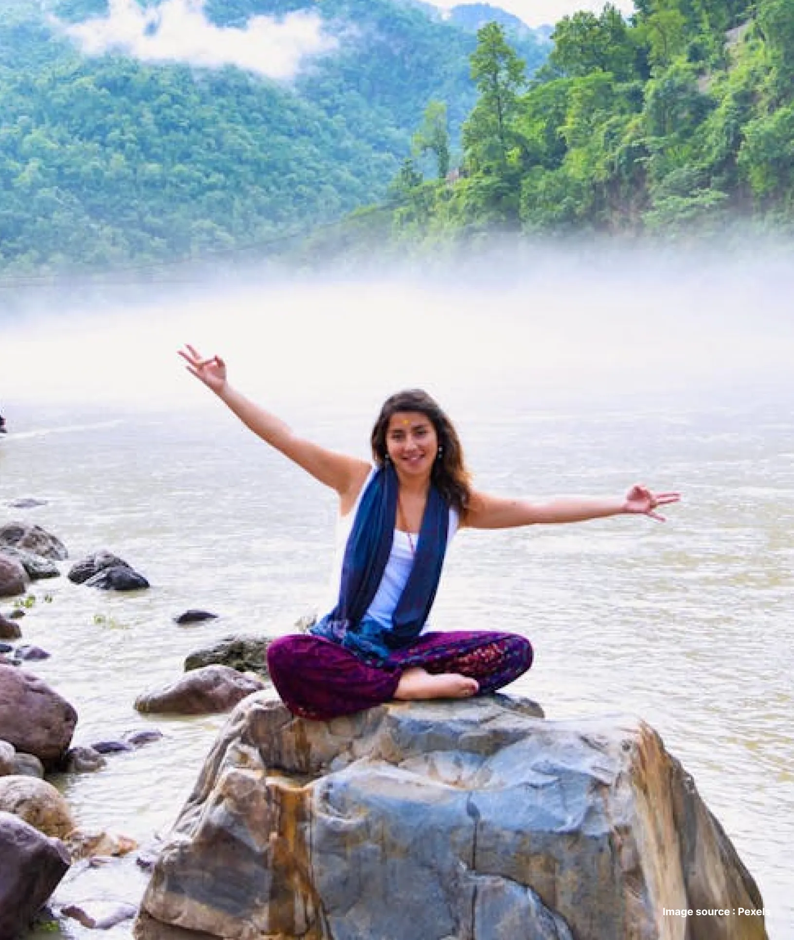 a woman joyfully poses in the himalayan foothills by the ganges river