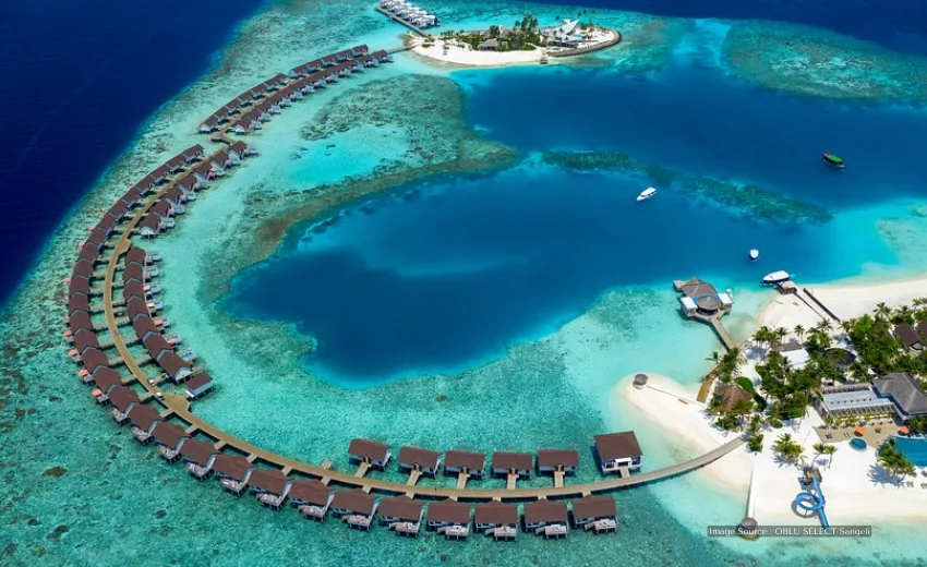 An aerial view of a luxury resort in the Maldives with overwater bungalows, a beach, and a swimming pool.