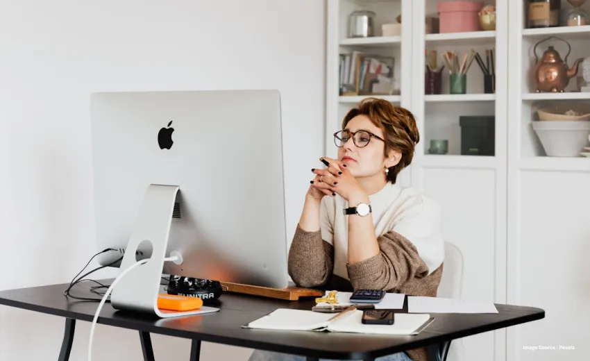 Woman wearing glasses sitting at a desk beside an Apple iMac