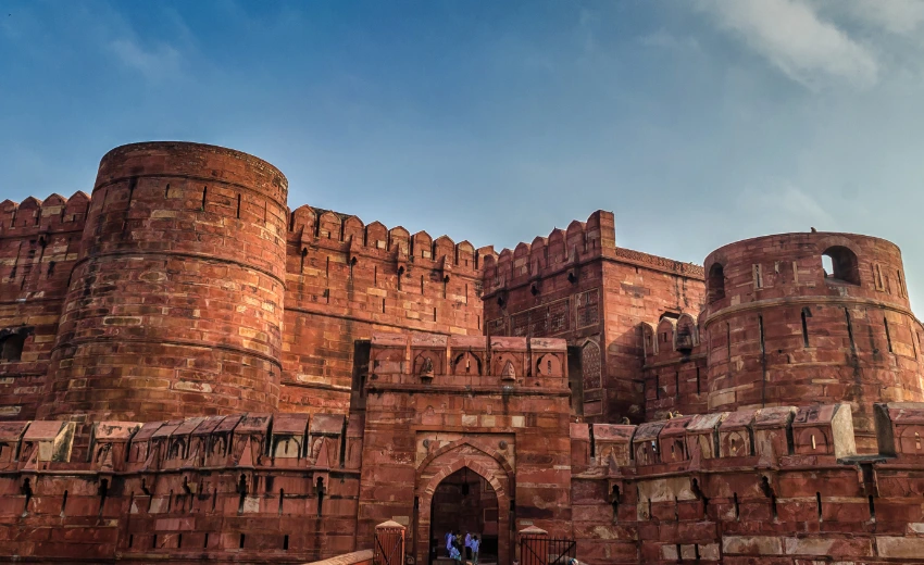 Agra Fort: "Taj Mahal group tour visiting historic Agra Fort, featuring massive red sandstone walls under a clear sky