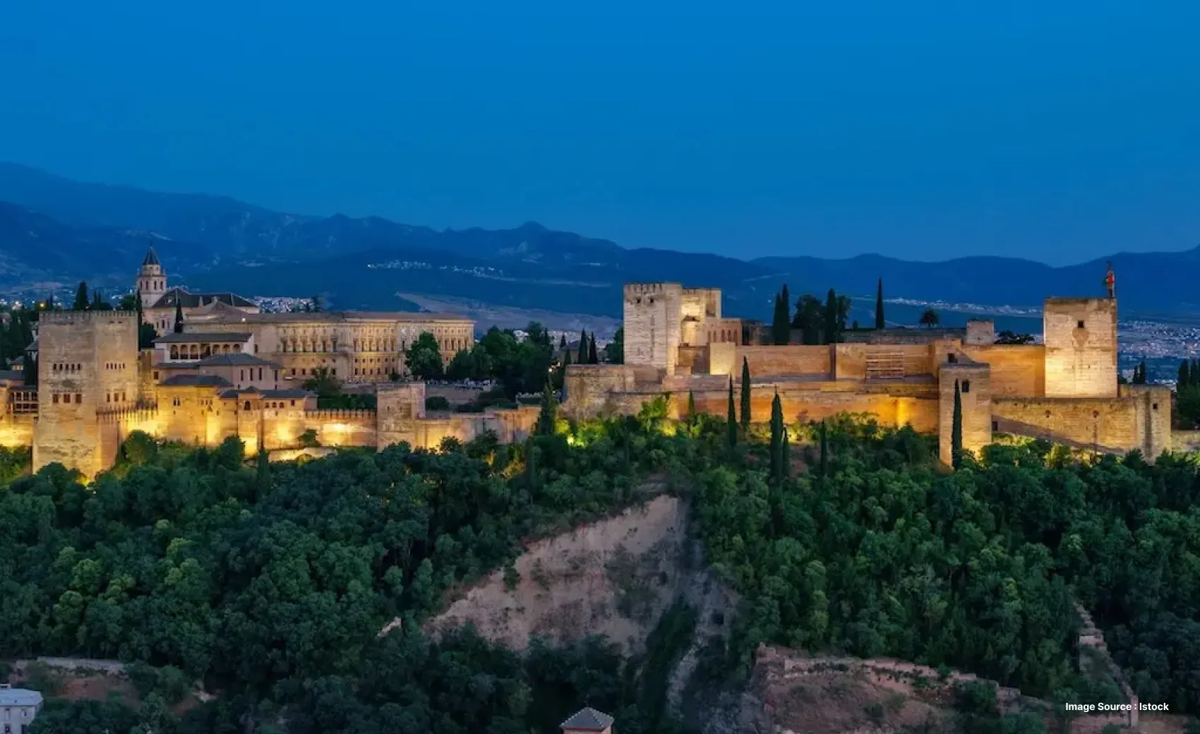aerial shot of alhambra palace lit up at night with dense greenery