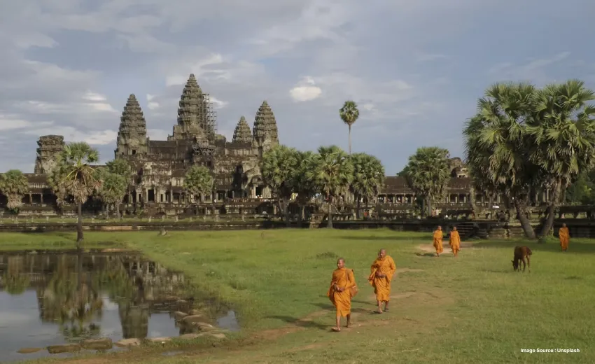 Ancient temple complex reflected in a pond, with monks walking nearby.