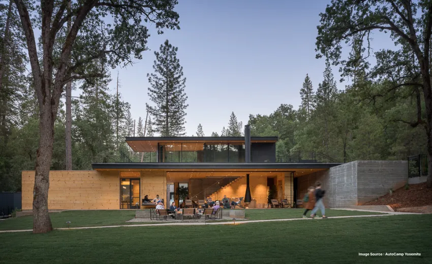 a modern looking two storey property with people lounging out in the front in midst of trees