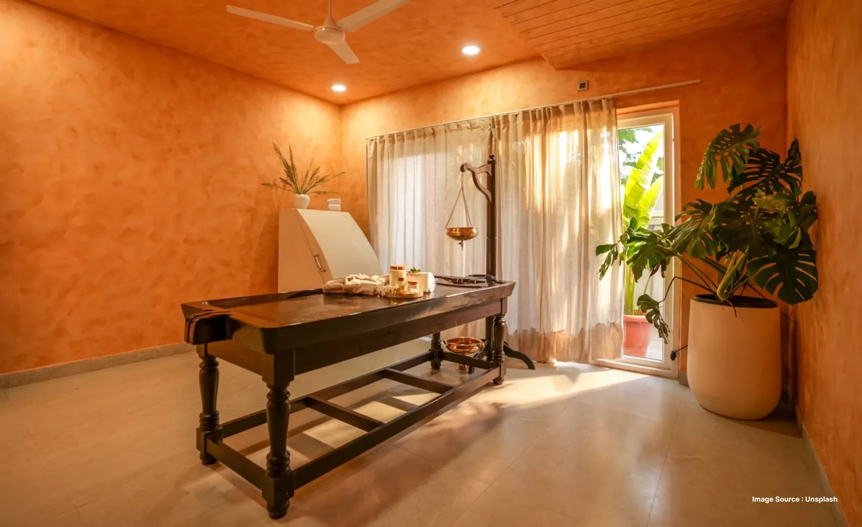 an orange walled-room with an ayurvedic spa setup with a pot of oil and medicial herbs on a bed