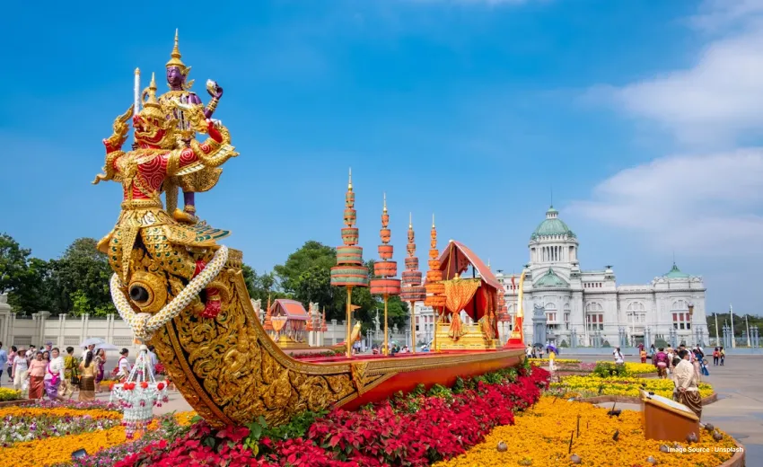 Ornate golden ceremonial boat sculpture in a flower-filled public square.