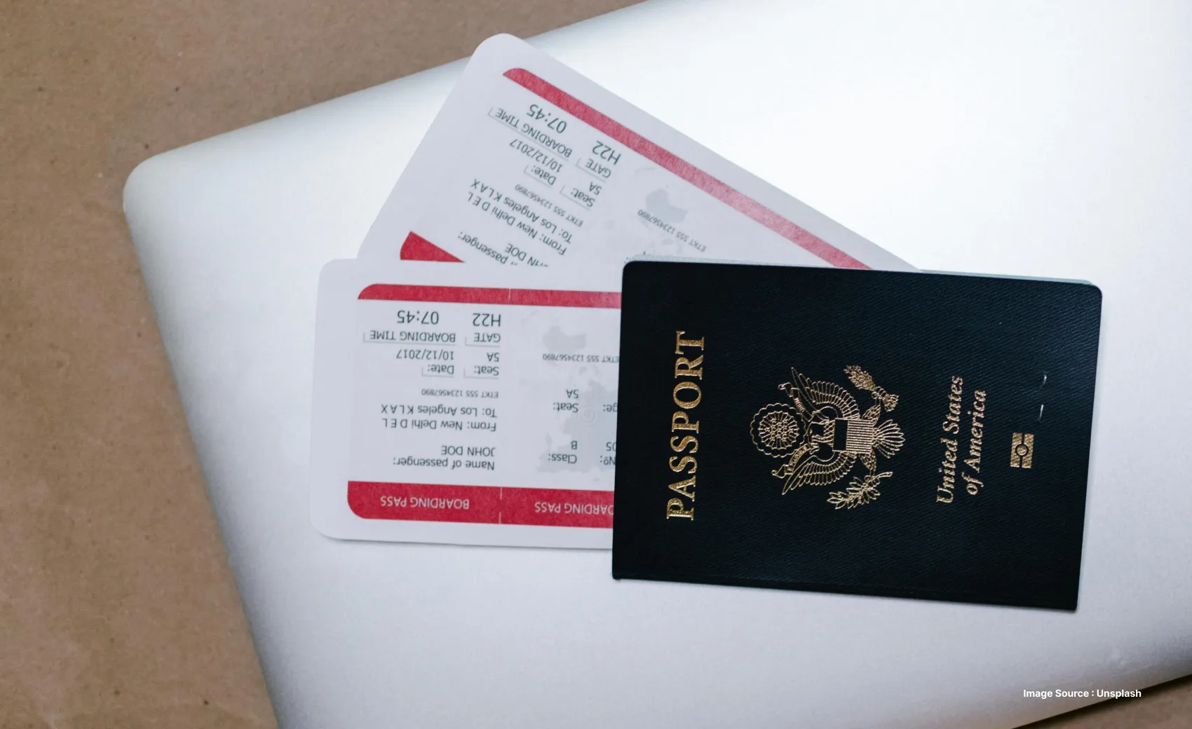two boarding passes lying on a silver laptop on a wooden surface with a usa passport