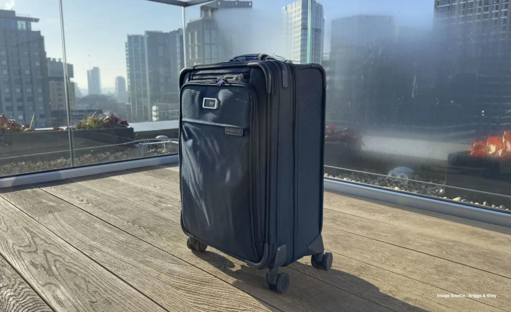a navy blue soft shell suitcase in a balcony with glass railings on wooden flooring