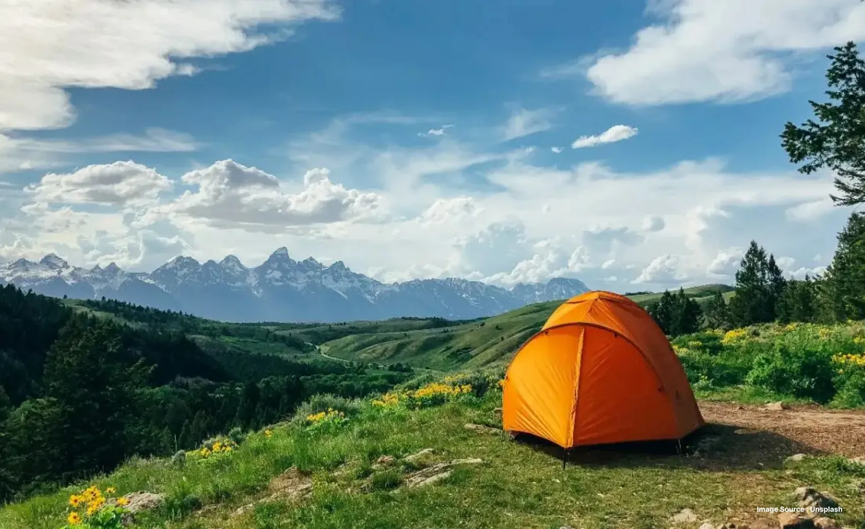 an orange tent set up with gorgeous view of green hills with distant mountains on a cloudy day