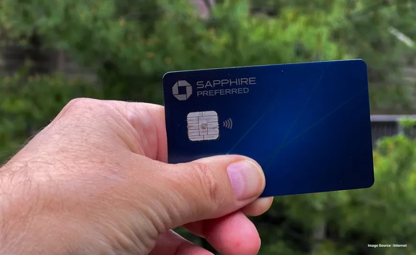 a person holding up the sapphire preferred card hiding the name with plants in the background