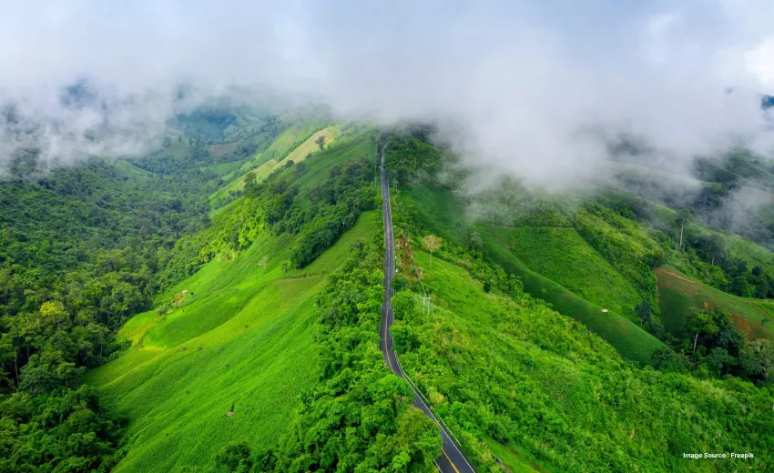 aerial shot of coorg with misty clouds as a road winds through 
