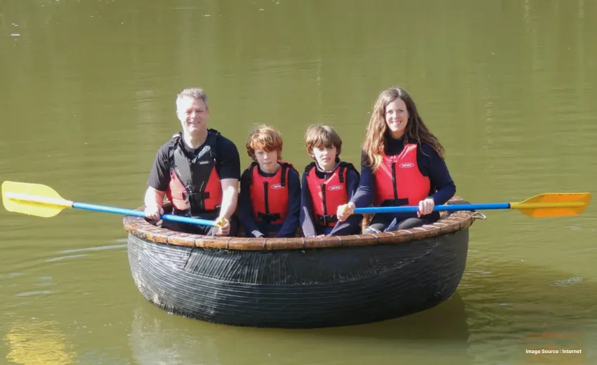 a white family with two kids in vests sitting in a coracle in the cauvery river