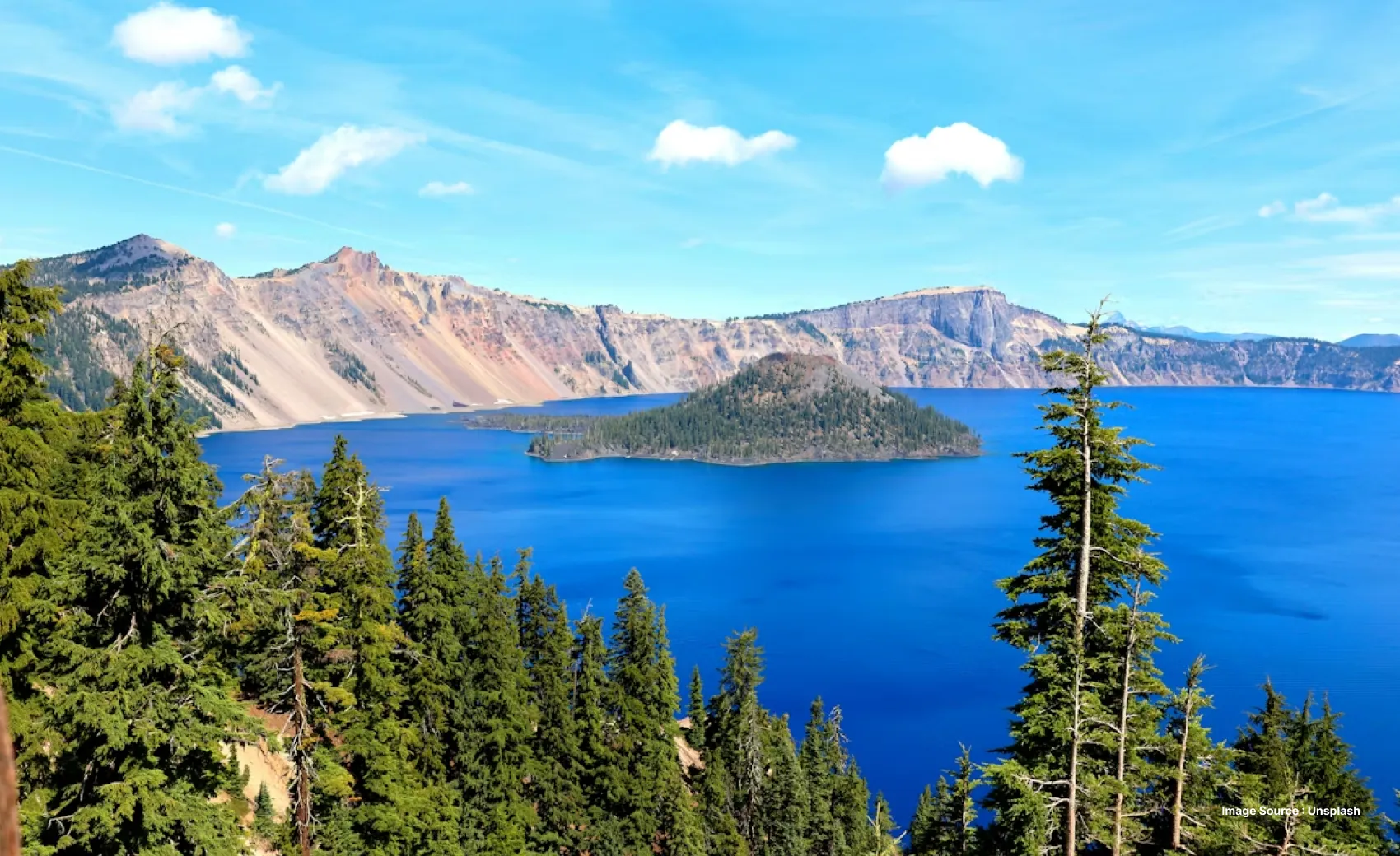 aerial shot of the blue waters of the crater lake surrounded by grey rugged hills and a pine tree jungle