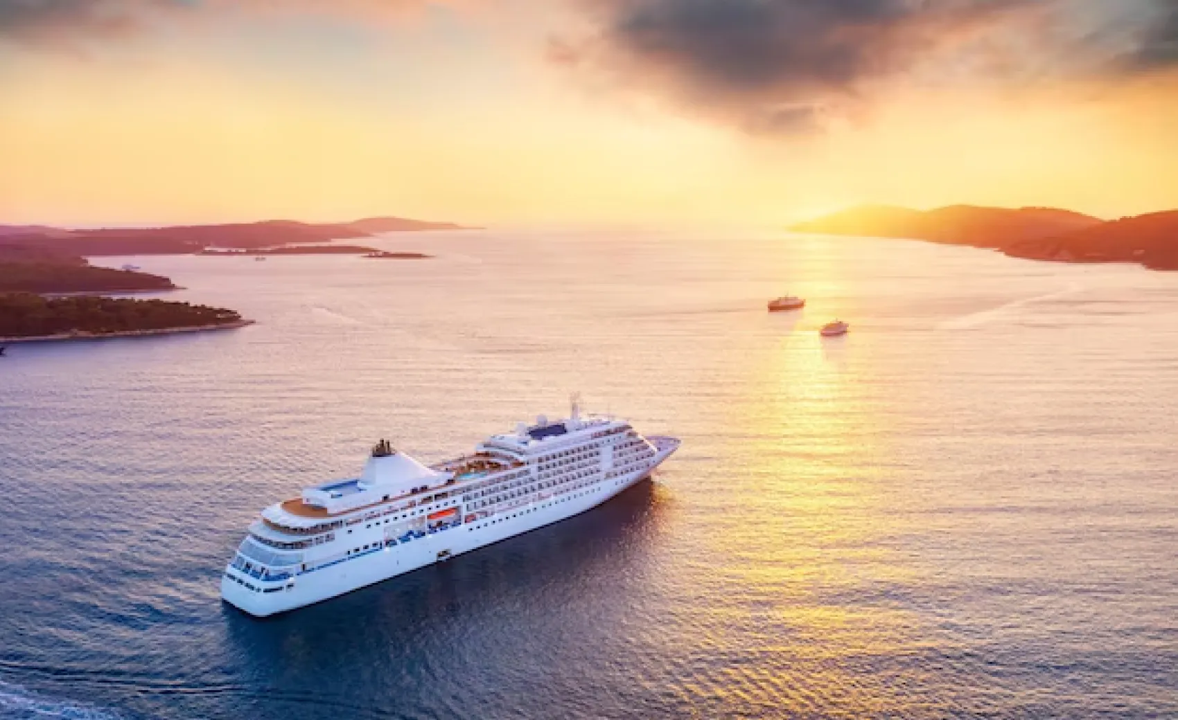 aerial shot of a white cruise ship and a few boats going ahead in water at sunset