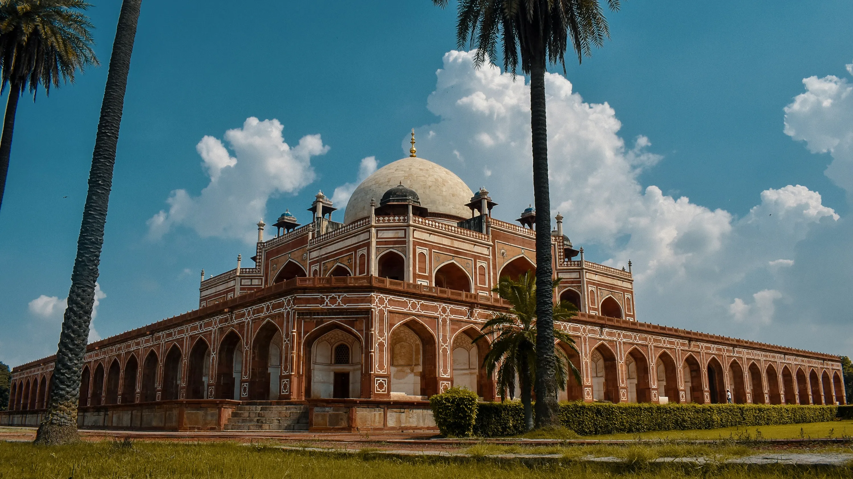 a side angle view of the humayuns tomb in delhi with palm trees and a clear sky