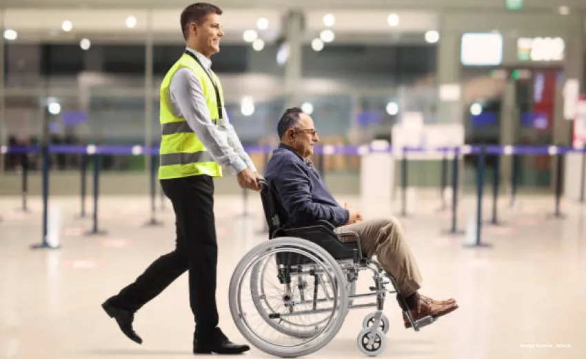 a uniformed airport staff with a neon reflector jacket pushing a wheelchair with a senior citizen