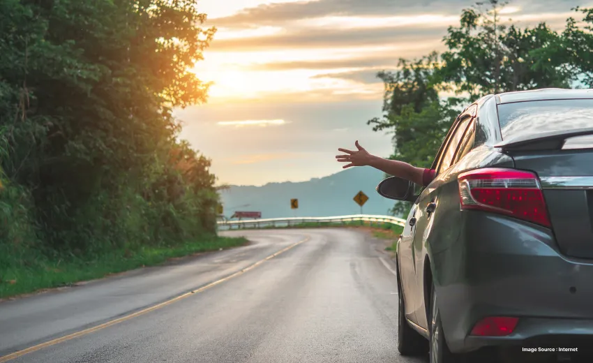a car driver sticks out their hand while driving on a beautiful empty road during sunset