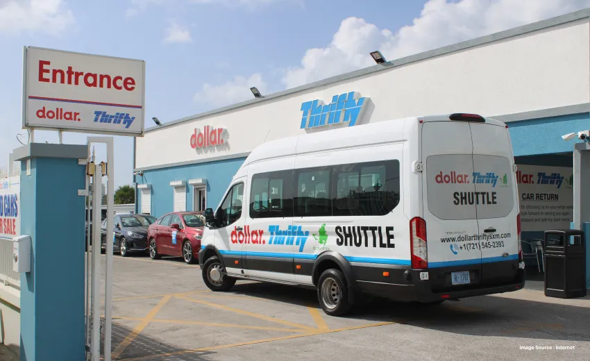a shuttle minivan parked outside a dollar/thrifty car rental store with other cars on the side