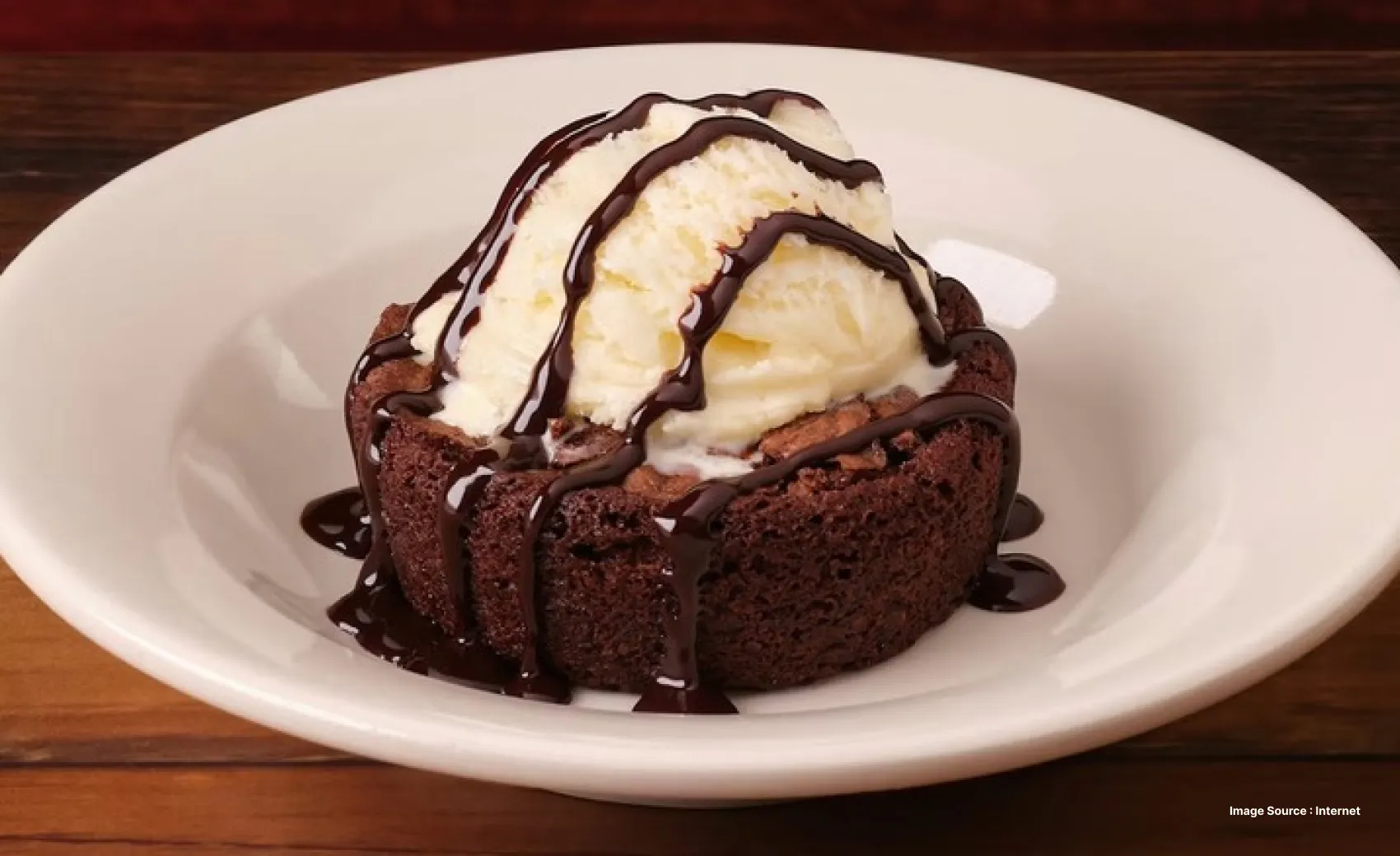 close up of a brownie served with a scoop of vanilla ice cream and a drizzle of chocolate syrup