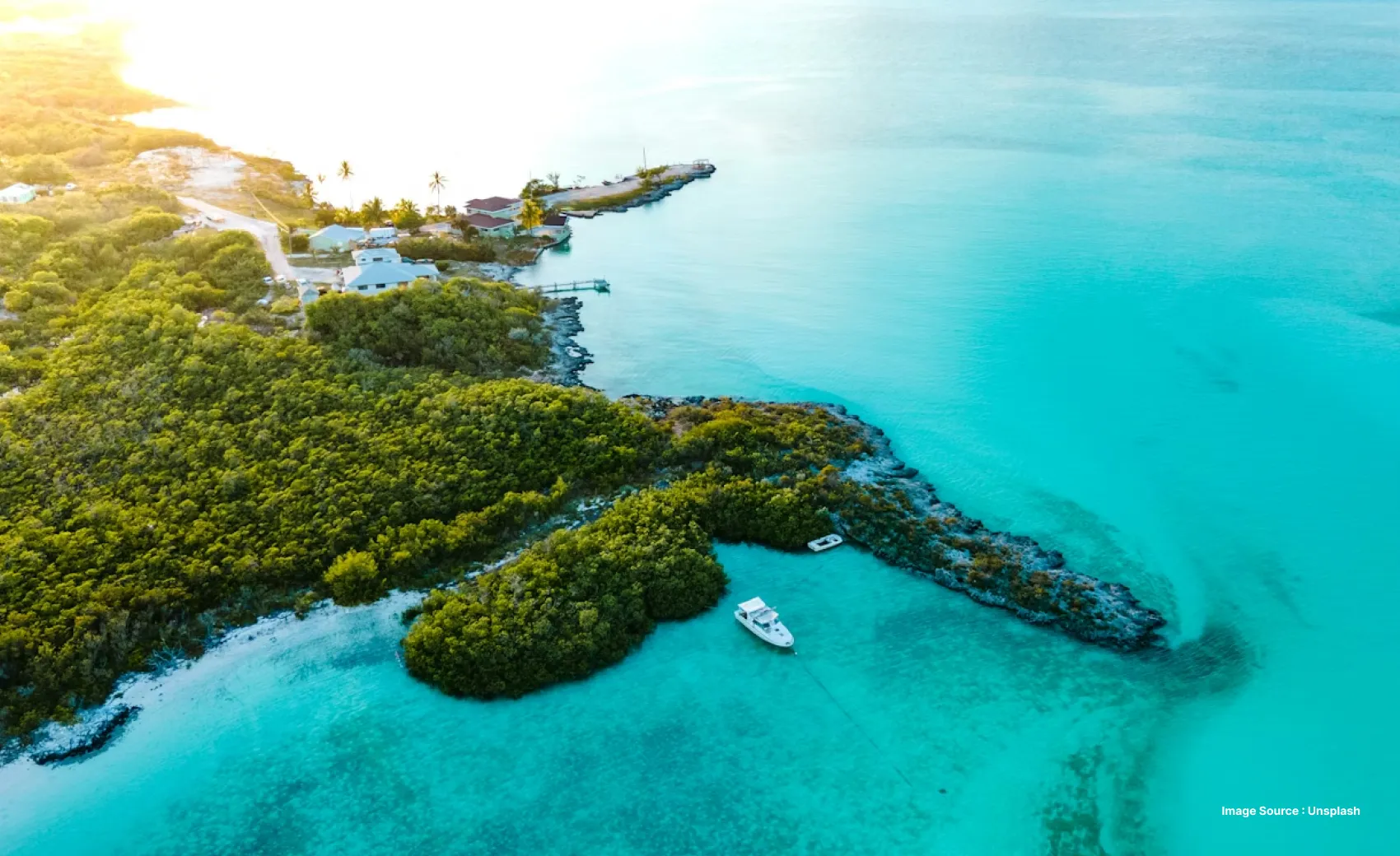 aerial shot of a lush green island with small hills and blue water with some yachts and buildings