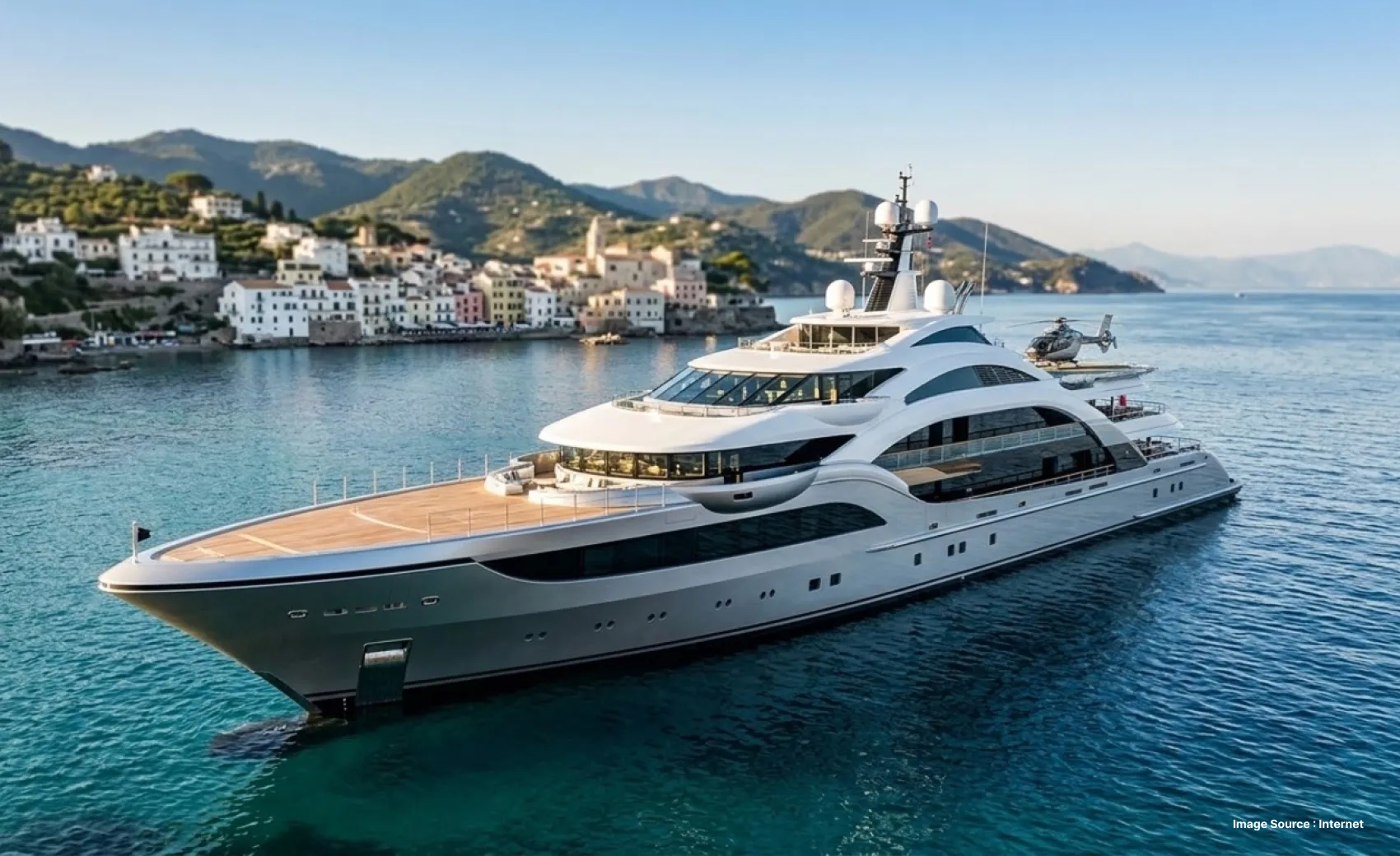 close up shot of the avanti super yacht with a beautiful coastline with hills and white buildings in the background