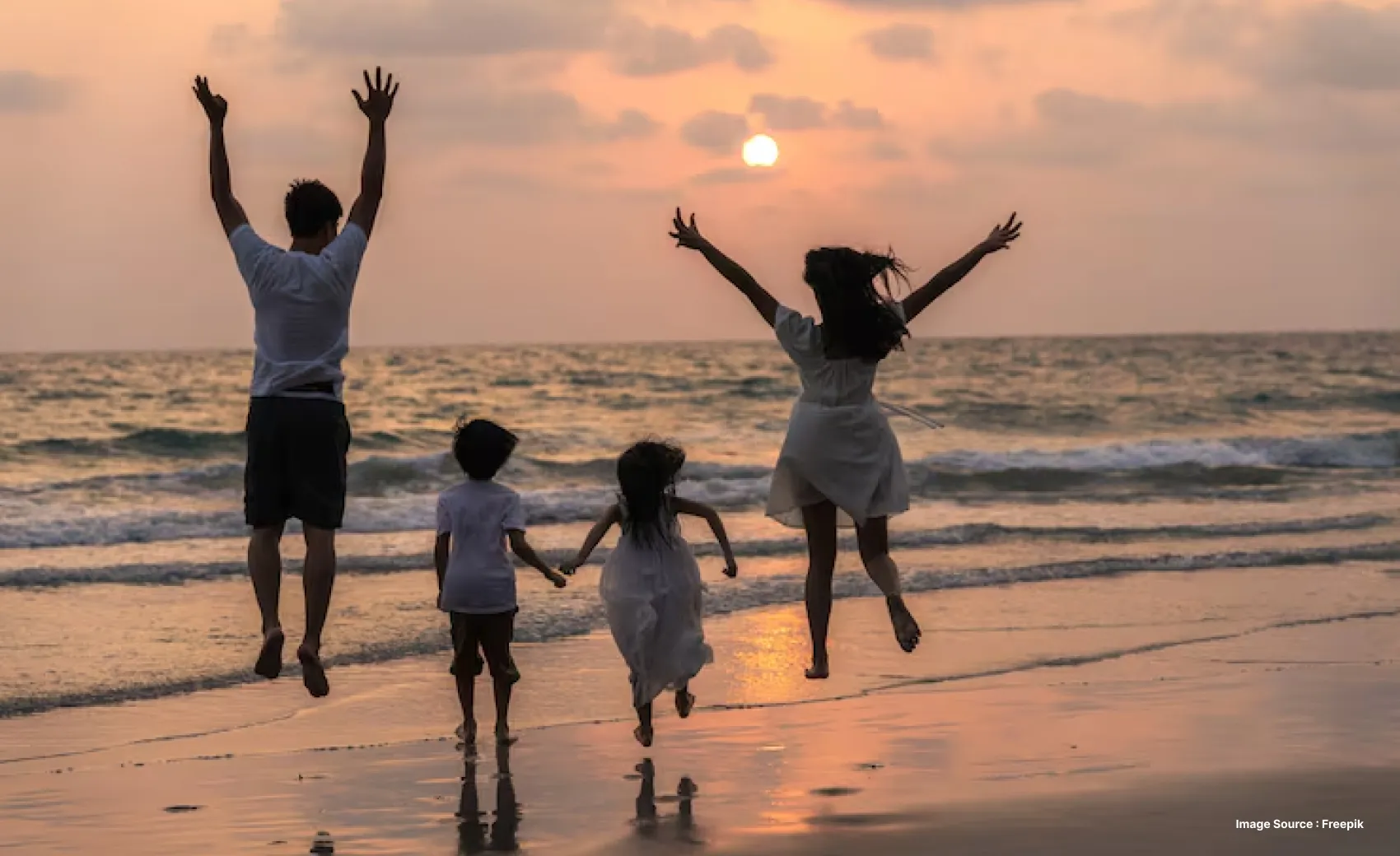 a family with two kids dressed in white jumping with joy at sunset on a beach