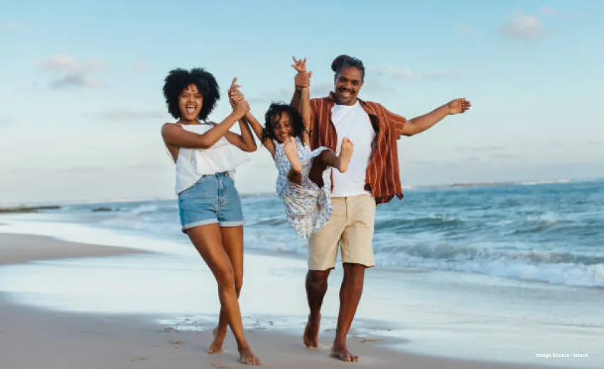 A black family enjoys on the beach close to the shore with their daughter