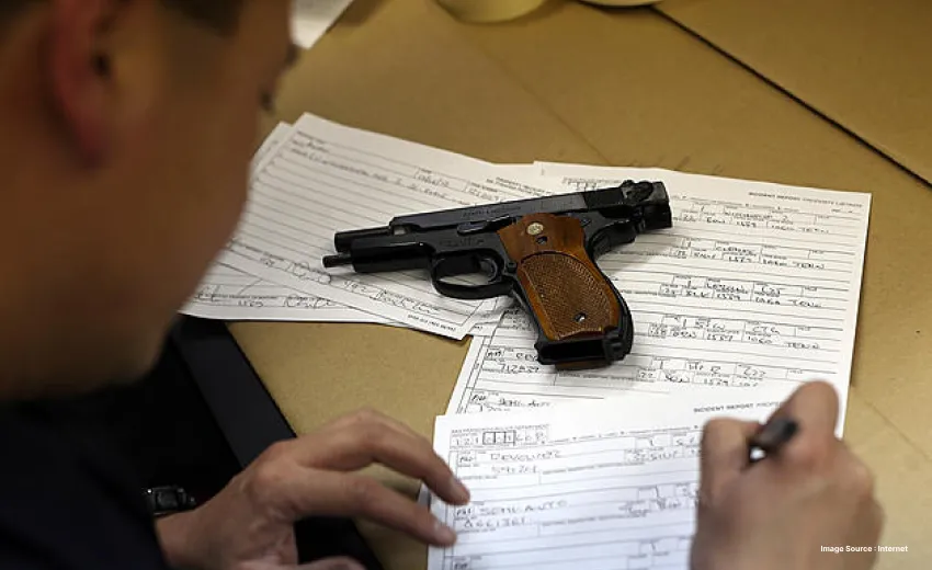 a pistol kept on a table on top of a few papers as a person fills a document