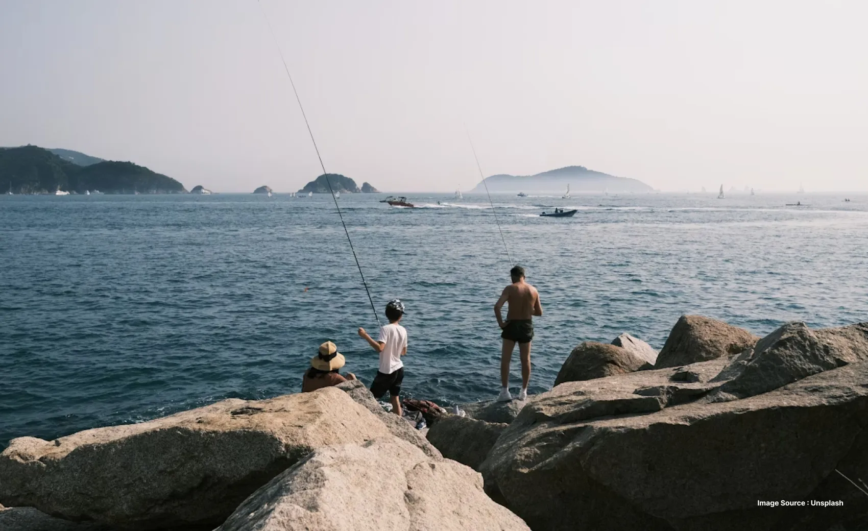 a family of three stands on huge rocks while fishing and enjoying the sun