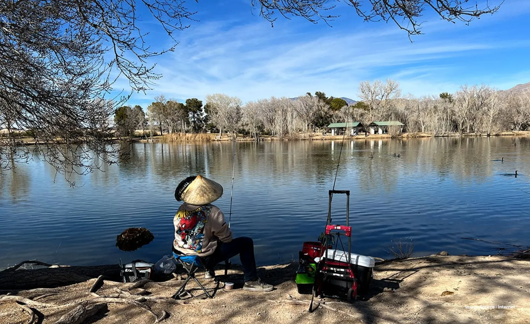 a man with a vietnamese wooden hat fishes at the pond on a sunny day