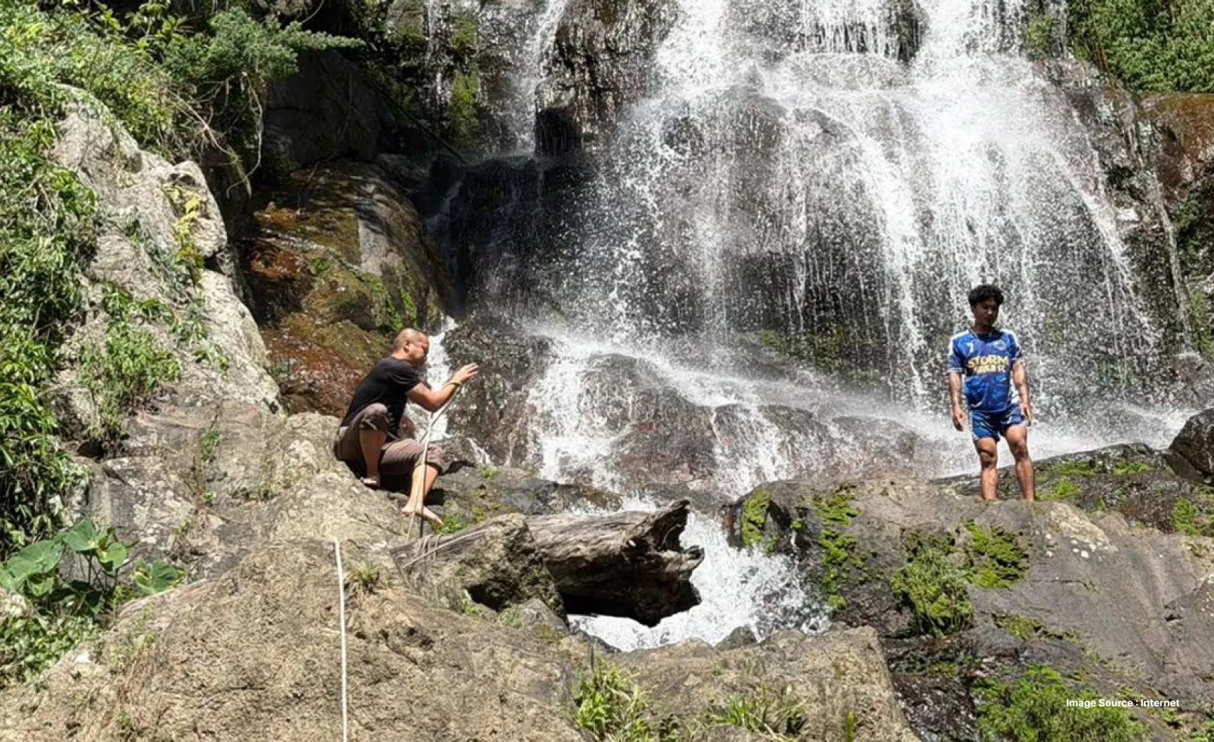 two men standing very close to a waterfall on the rocks