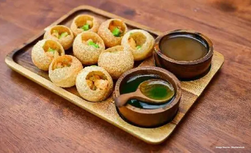 a bunch of pani puri with potato filling served on a wooden plate with green spicy water