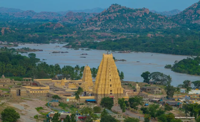 aerial shot of a golden towering temple in front of a river and small rugged hills