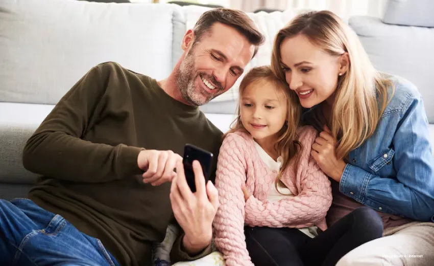 a family of three looking at their phone and smiling sitting close together