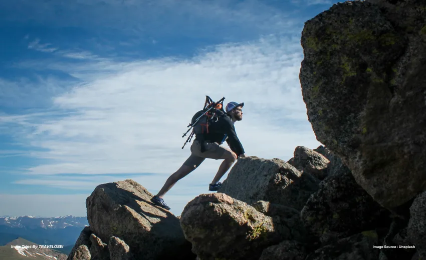 A man hiking on a mountain with a dry bag on his back standing in between two rocks