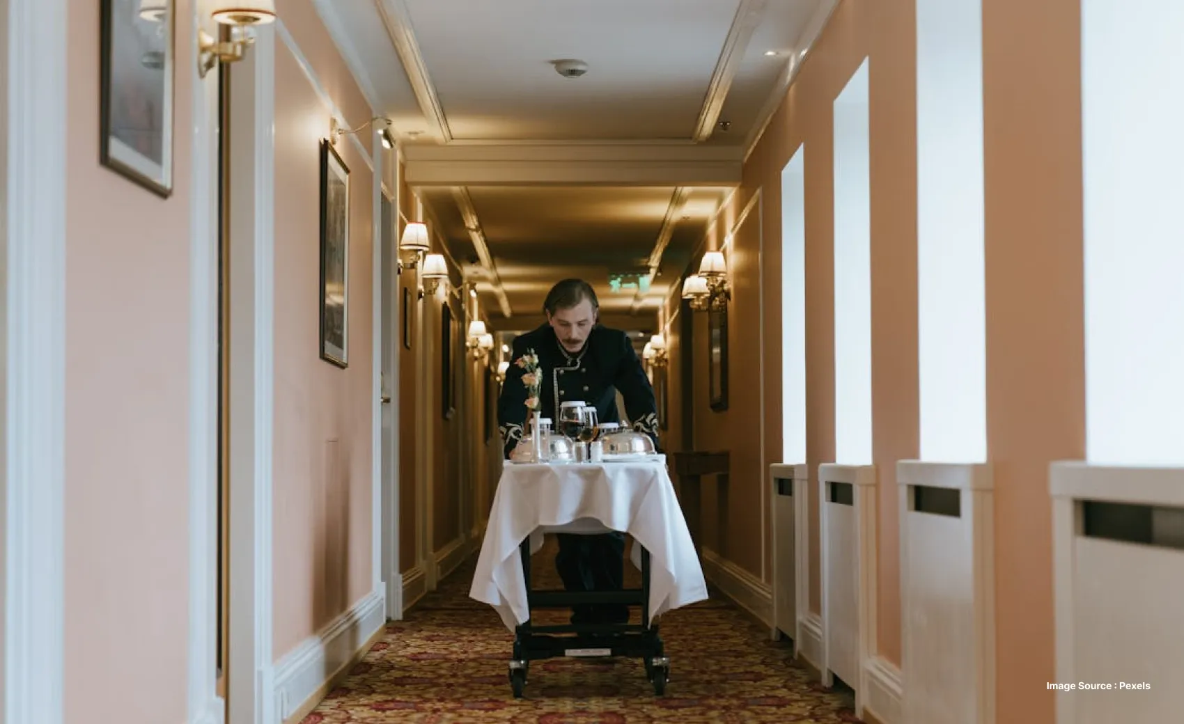 a uniformed hotel staff pushes a food trolley down a hotel lobby