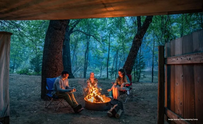 three adults enjoying a bonfire outside a camp in a dense forest