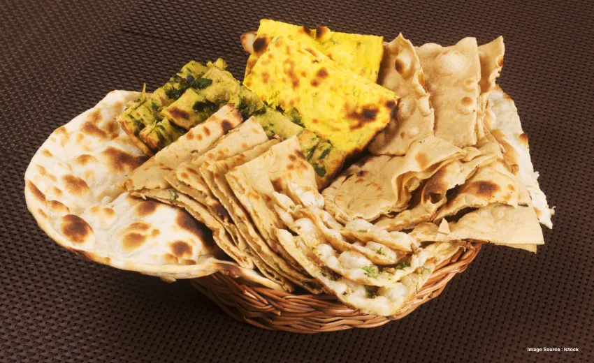 a basket with different sorts of indian breads including naan, paratha and missi roti