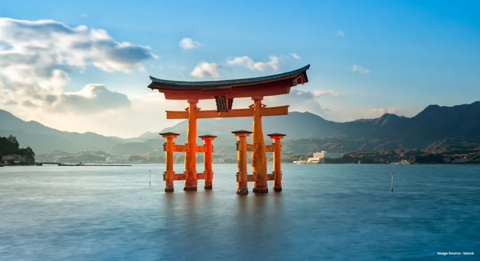 an orange japanese gate floating in middle of an ocean surrounded distantly with green hills