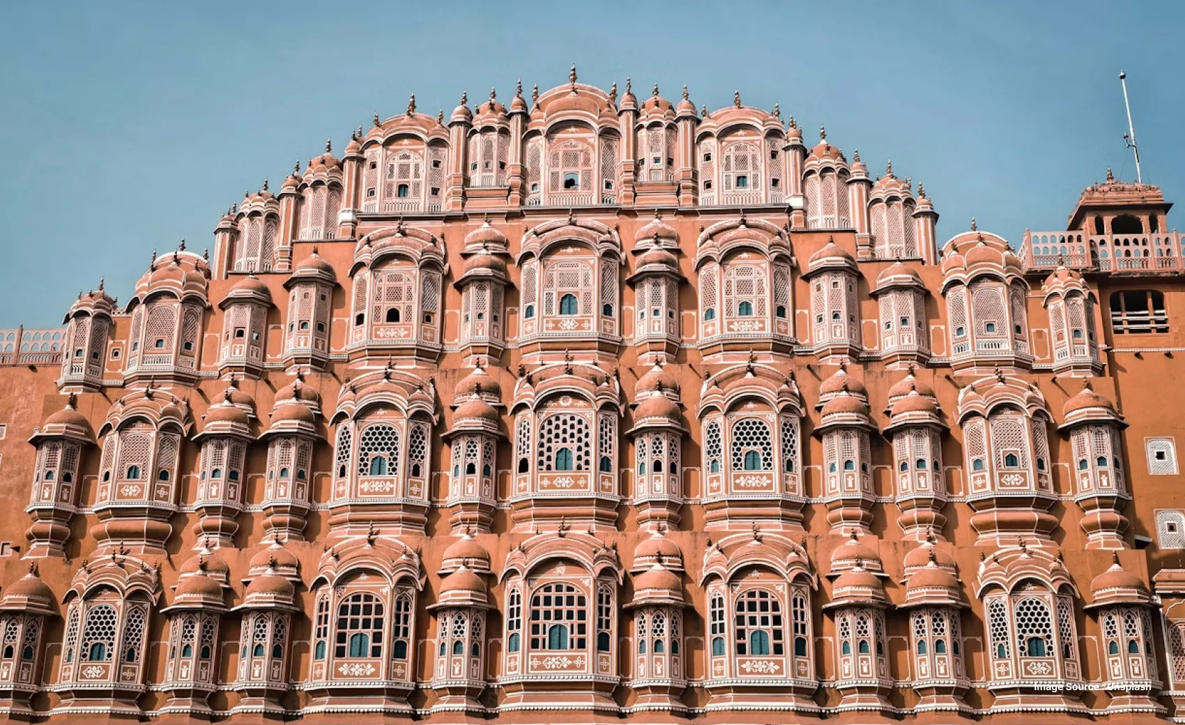a close up shot of the iconic hawa mahal in jaipur with a pink building and intricately carved tiny windows