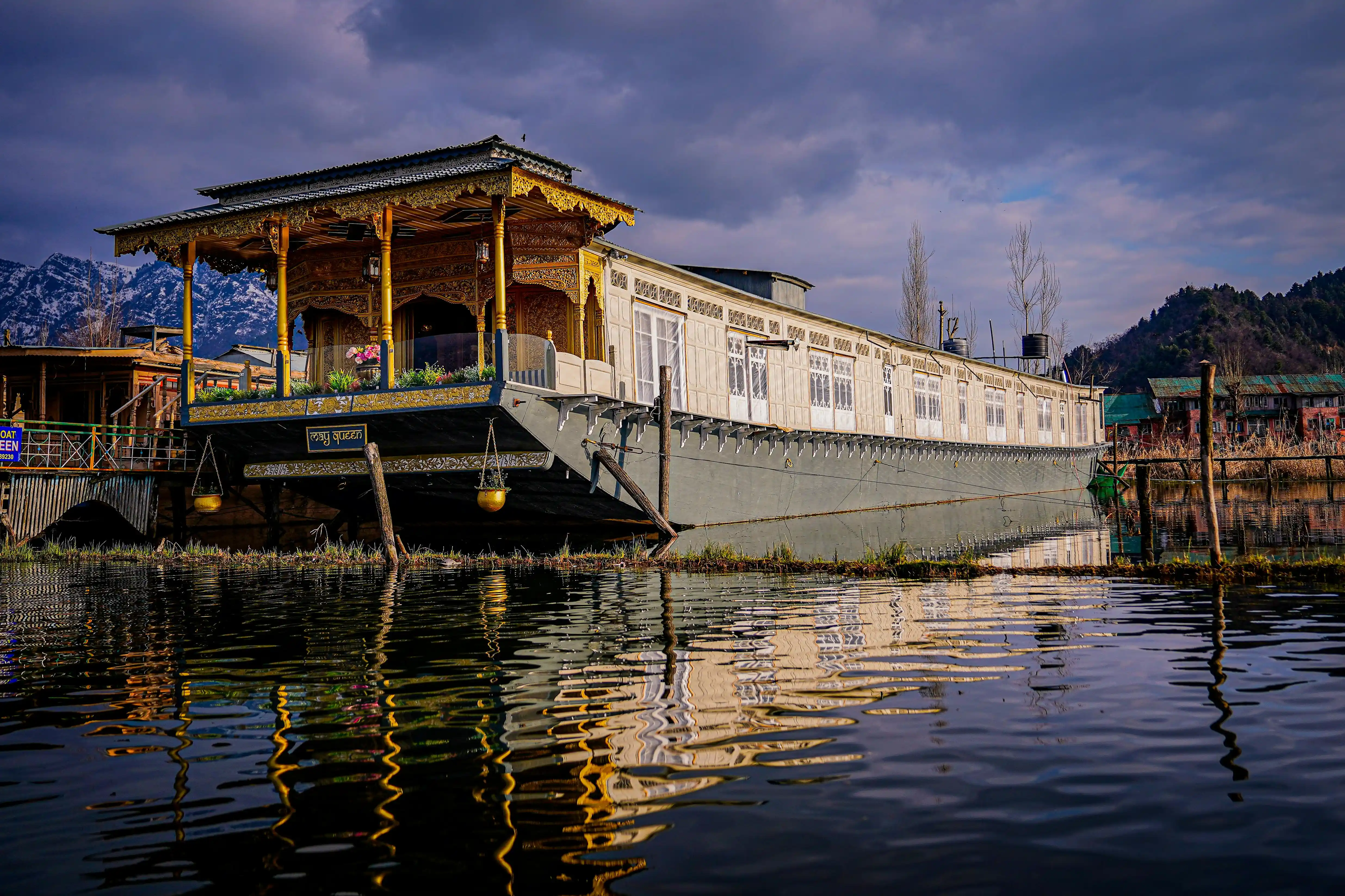 a traditional houseboat in srinagar with intricate and colorful carvings on its facade with snow capped peaks
